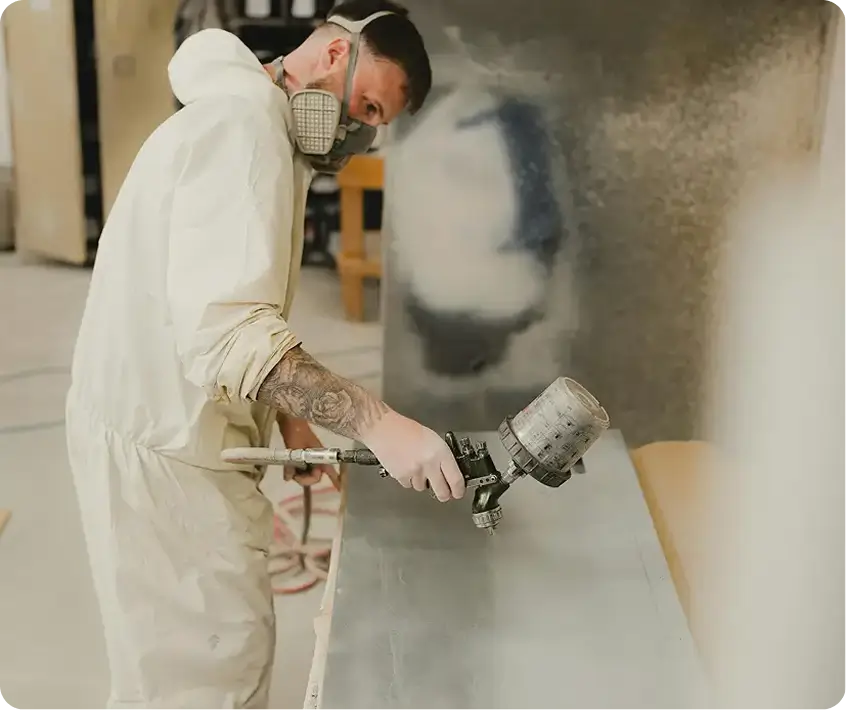 A technician in a respirator sprays paint using a spray gun