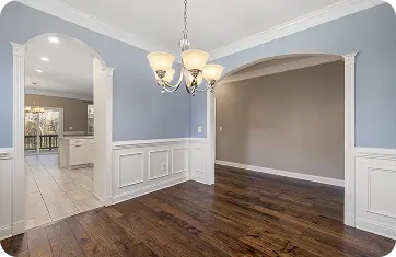 Elegant dining room with polished dark hardwood floors, light blue walls, and classic wainscoting.