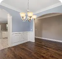 Empty dining room highlighting polished dark hardwood flooring, blue walls, and elegant white wainscoting