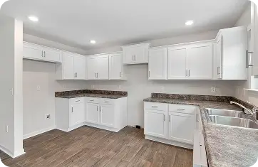 Newly remodeled empty kitchen with clean white cabinetry, dark countertops, and wood-look laminate floors